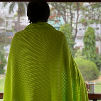 Person wearing a neon yellow chunky knit throw looking out of a balcony with a garden view.