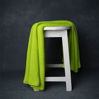 Chunky knitted neon yellow organic cotton throw blanket draped over a white stool against a dark background.