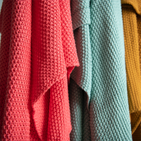 Three chunky knitted throws in red, blue, and mustard pictured next to each other.
