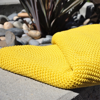 Yellow textured knitted cotton throw on a stone surface with succulent plants and pebbles in the background.