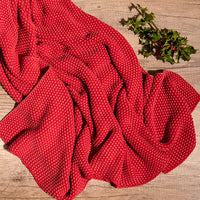 Red knitted washed moss cotton throw blanket on a wooden surface with Christmas mistletoe.