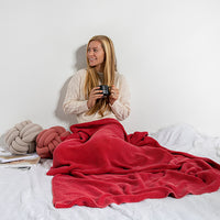 Woman sitting on a bed with a red washed moss cotton throw blanket and holding a mug, smiling.