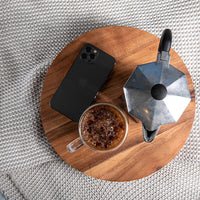 Wooden tray with a cup of coffee, phone, and metal coffee pot placed on an off white textured organic cotton throw.