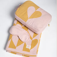 Folded pink and yellow patterned blanket with matching case and eye mask on a light gray background.