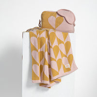 Folded organic cotton travel blanket with heart pattern and matching pouch on a white background.