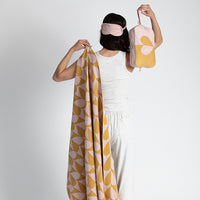Person holding a patterned orange and pink travel blanket and pink pouch with a heart against a white background
