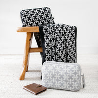 Soft black and white organic cotton travel blanket with a chain design placed on a chair with a travel journal.
