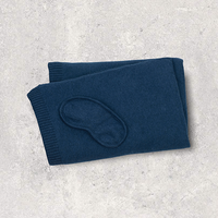 Folded navy blue travel blanket and matching eye mask on a light gray surface.