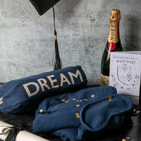 Navy blue travel blanket set with 'DREAM' text, moet champagne bottle, and graduation card on a textured surface.
