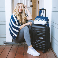 Woman sitting on a step with a black suitcase and a blue and white travel pouch with 'XOXO' text.