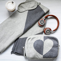 Gray and white patterned pouch with heart design, retro headphones, take-out coffee and a blanket on a light background
