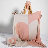 Woman holding a large pink and beige blanket with a dual tone heart design on a white background