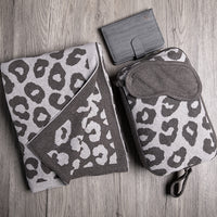 Brown leopard print travel set including a blanket, pouch, and eye mask on a wooden surface with a card holder.