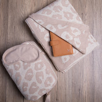 Linen coloured leopard print folded blanket and pouch with a brown leather card holder on a wooden surface.