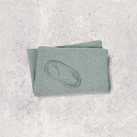 Folded organic cotton light grey travel blanket with matching eye mask on a textured gray surface.