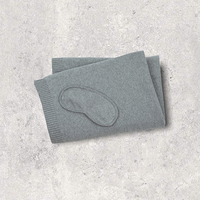 Medium grey eye mask and folded organic cotton blanket on a textured gray surface.