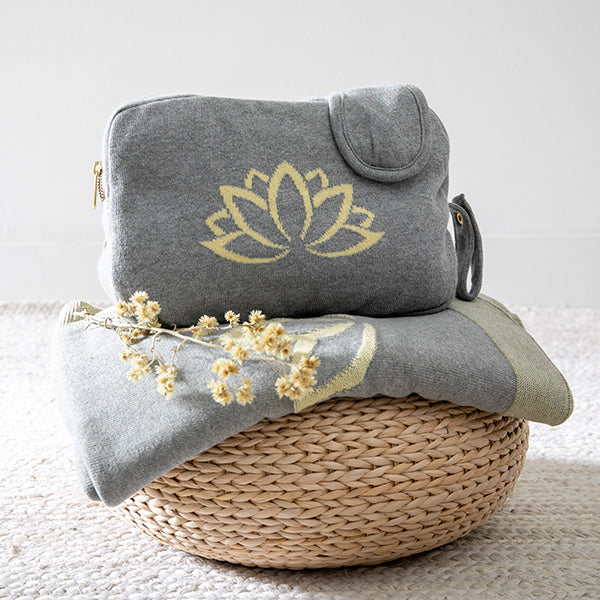 Gray pouch with yellow lotus design and matching folded blanket on a woven basket with dried flowers.