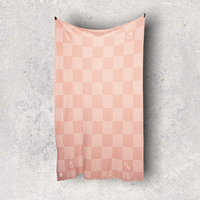 Pink checkered cotton travel blanket hanging on a gray textured background