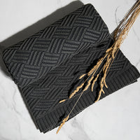 Dark gray chunky knit cotton blanket with a geometric brick pattern with wheatgrass on a light background.