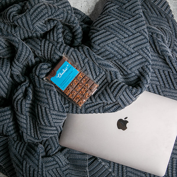 Apple laptop under a textured washed navy mel chunky knit cotton blanket with a chocolate bar on top.