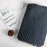 Navy mel moss-knit cotton throw blanket with a card addressed to dad and small cupcake on a marble surface.