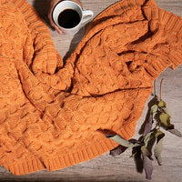 Washed orange curvy knit throw blanket on a wooden surface with a cup of coffee.