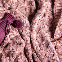 Close-up of a pink curvy knitted cotton blanket with a purple knitted wine sleeve.