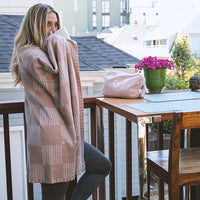 Woman holding a checkered pink blanket on a balcony with a table and bright pink flowers in the background