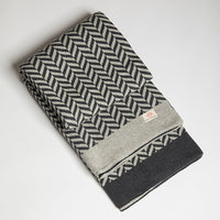 Grey folded organic cotton blanket with a herringbone pattern on a light gray background.