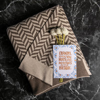Folded dark brown and beige patterned cotton throw blanket with a birthday card addressed to Grandpa.