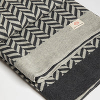 Folded dark grey organic cotton throw with a geometric herringbone pattern and a 'Pink Lemonade' brand label.