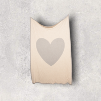Neutral coloured cotton travel blanket with grey border heart design hanging on a wall.