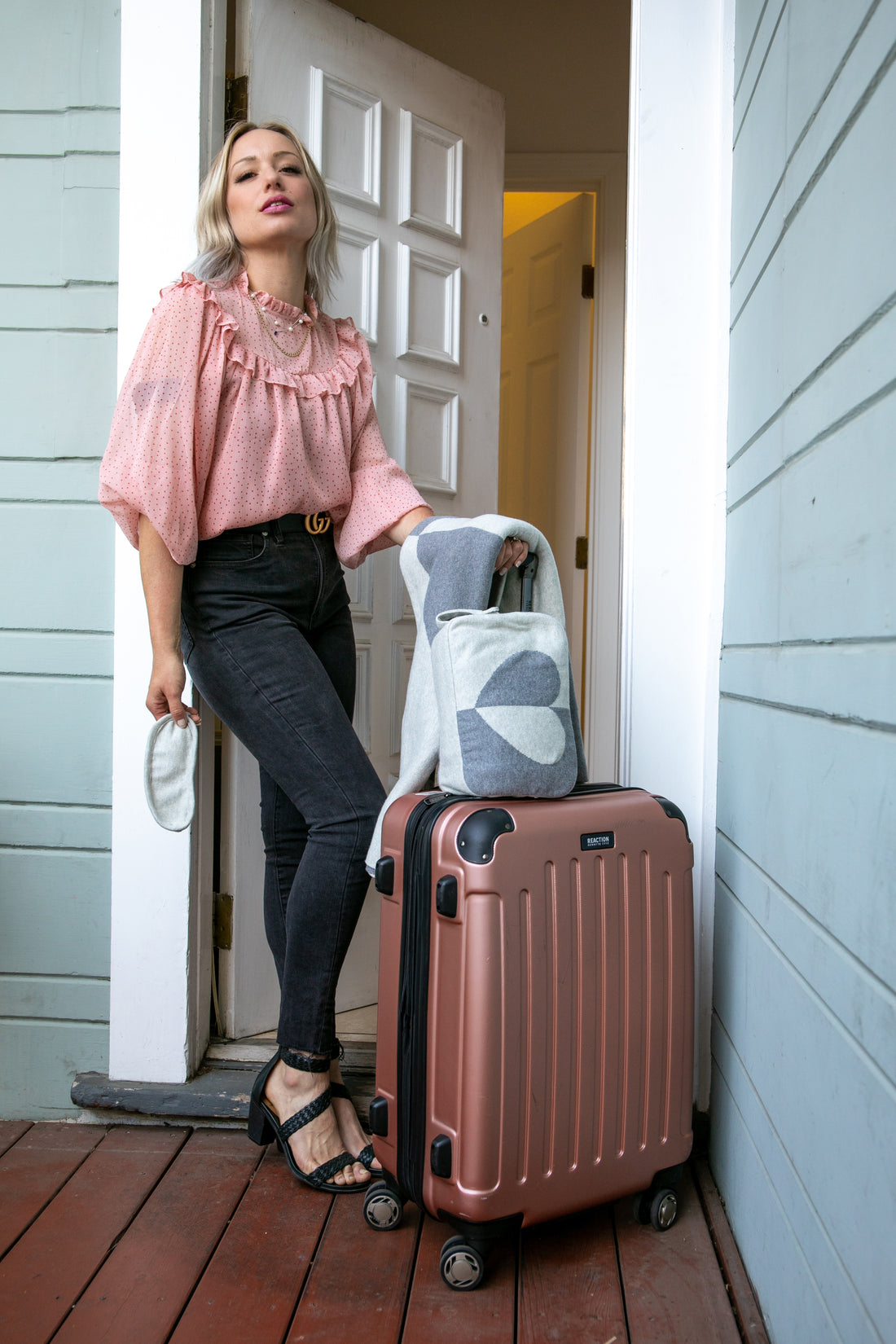 A person standing next to a suitcase with a travel pouch, featuring a two-tone heart pattern in shades of grey.