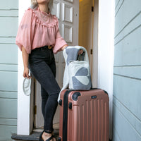 A person standing next to a suitcase with a travel pouch, featuring a two-tone heart pattern in shades of grey.