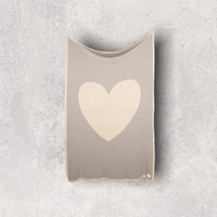 Grey cotton travel blanket with a beige heart and border hanging on a wall.