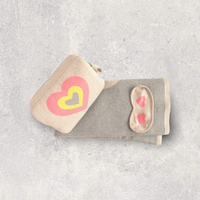 Compact travel organiser bag with a multi-color heart design, containing a folded organic cotton blanket and eye mask with hearts.
