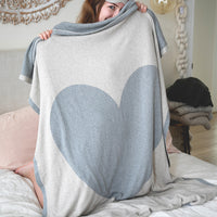 Woman holding up a luxurious beige cotton travel blanket with a grey heart and border.