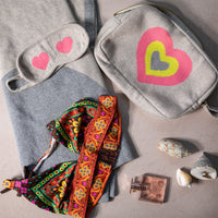 Flat lay of the Crazy Hearts organic cotton travel set, highlighting the soft blanket, eye mask, and multi-color heart zip pouch with other travel accessories.