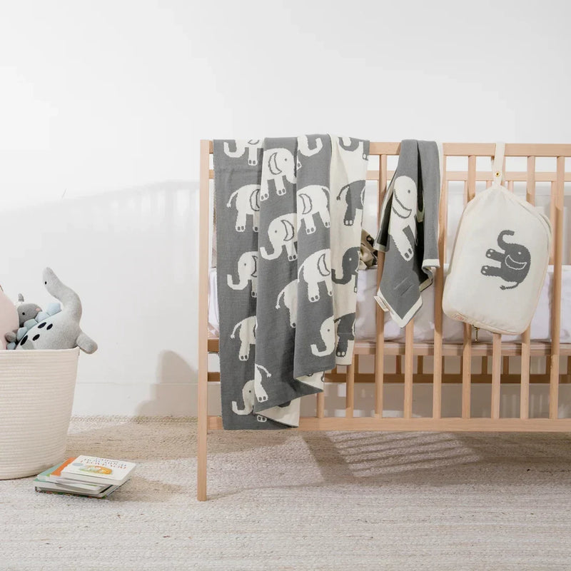 Pink Lemonade Elephant Love baby blanket and burp cloth set draped over a wooden crib.