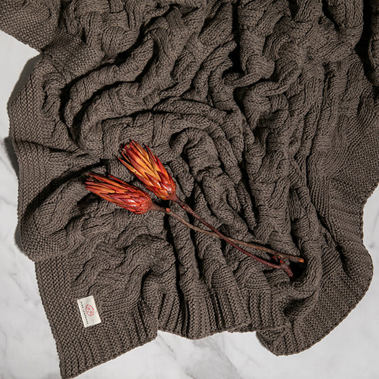 Pink Lemonade Drapa organic cotton knit throw blanket in charcoal styled with dried red flowers.