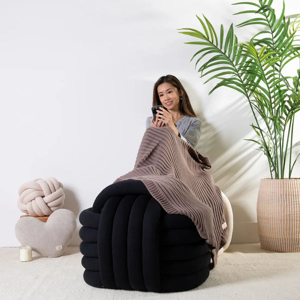Pink Lemonade black knotted pouf styled beside a lounge chair for a cozy spring home.