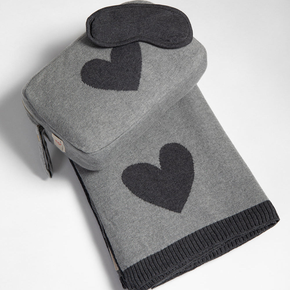 Gray travel blanket with black heart pattern and matching eye mask on a white background