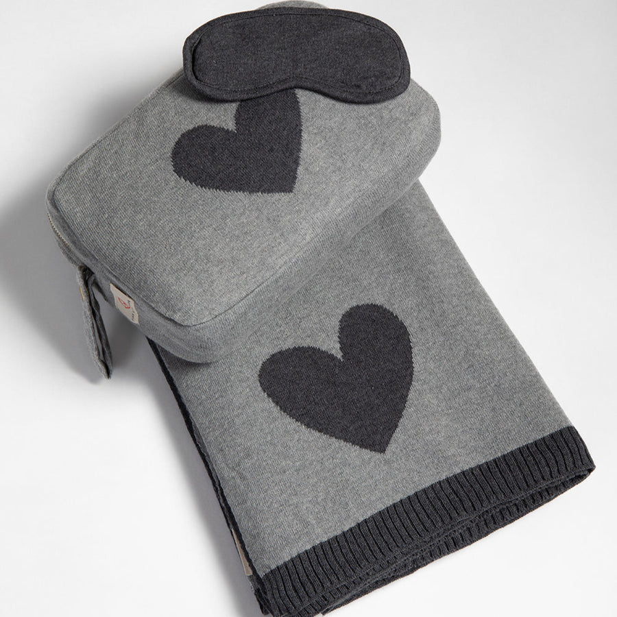 Gray travel blanket with black heart pattern and matching eye mask on a white background