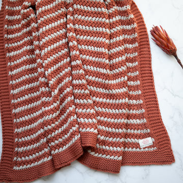 Organic cotton throw woven in horizontal stripes of rust and linen