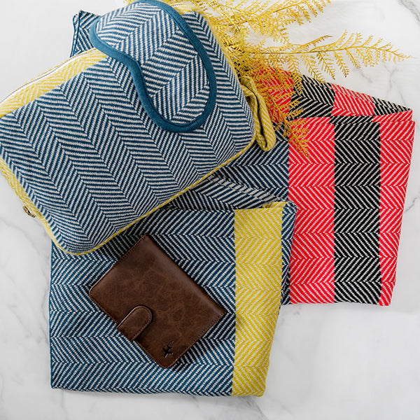 Set of a chevron cotton travel blanket, eye mask and zip bag with a wallet on a white surface