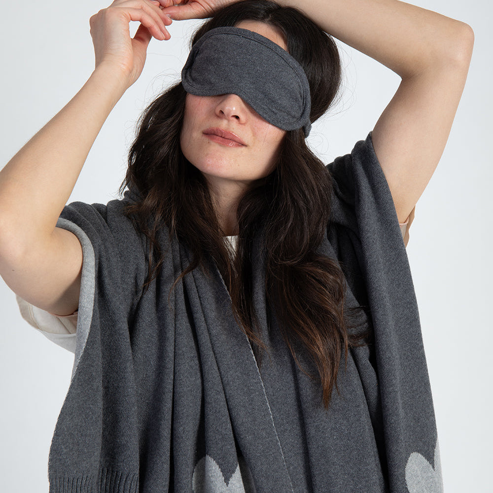 Lady wearing a gray eye mask and gray blanket with heart patterns on a white background