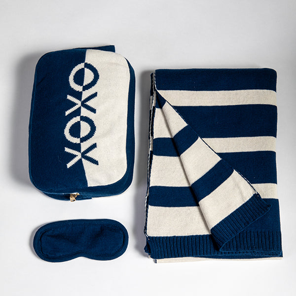 Navy and white striped blanket with XOXO pouch and eye mask on a light gray background