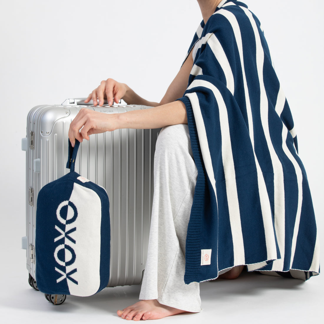Person holding a silver suitcase with a navy and white bag featuring 'XOXO' design, wearing a blue and white striped blanket.