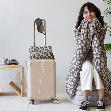 Woman wrapped in a leopard print travel blanket next to a suitcase with a leopard print pouch