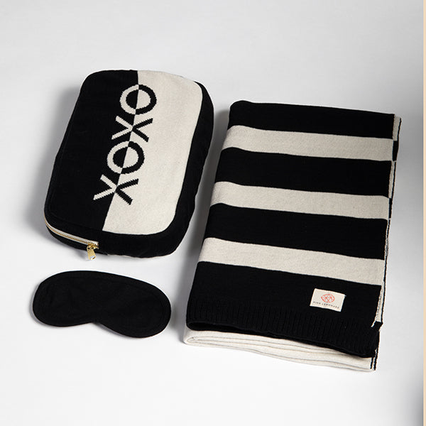 Black and white striped blanket with 'XOXO' pouch and eye mask on a light gray background